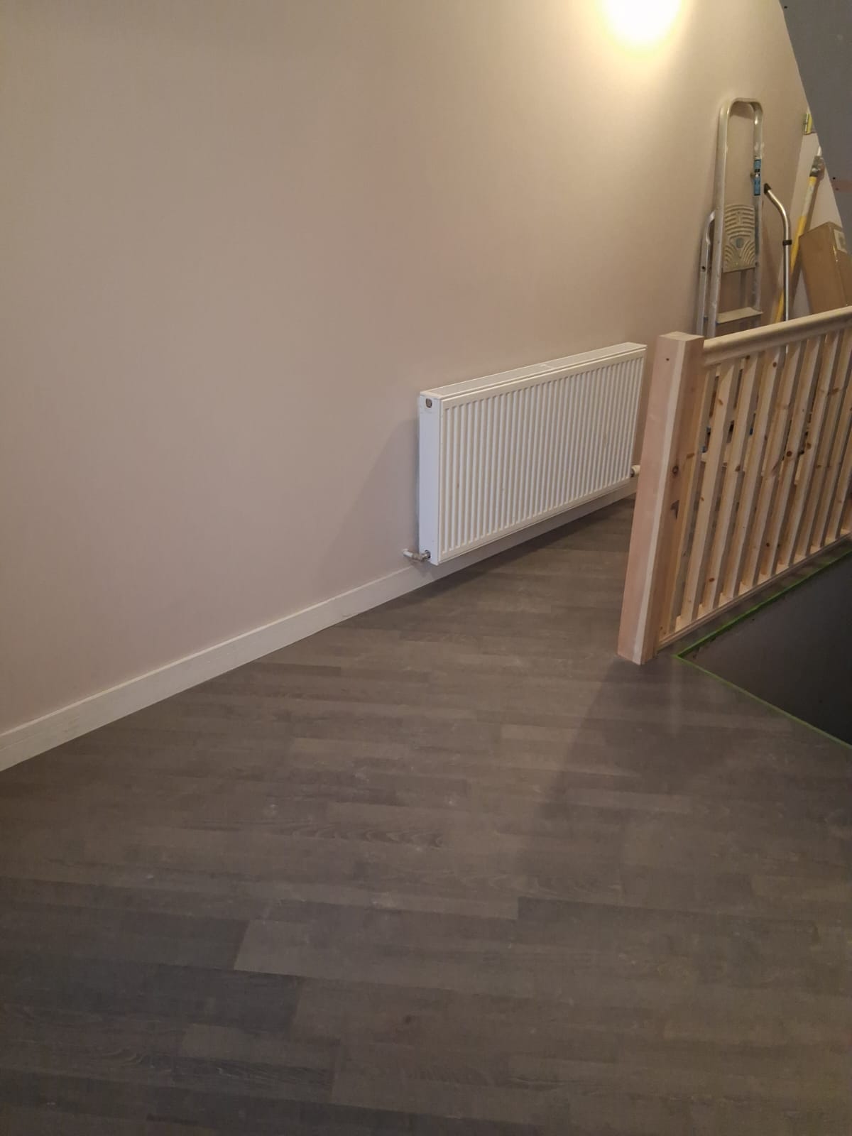 Hardwood floor running along a landing beneath a white radiator, beside a timber stair balustrade
