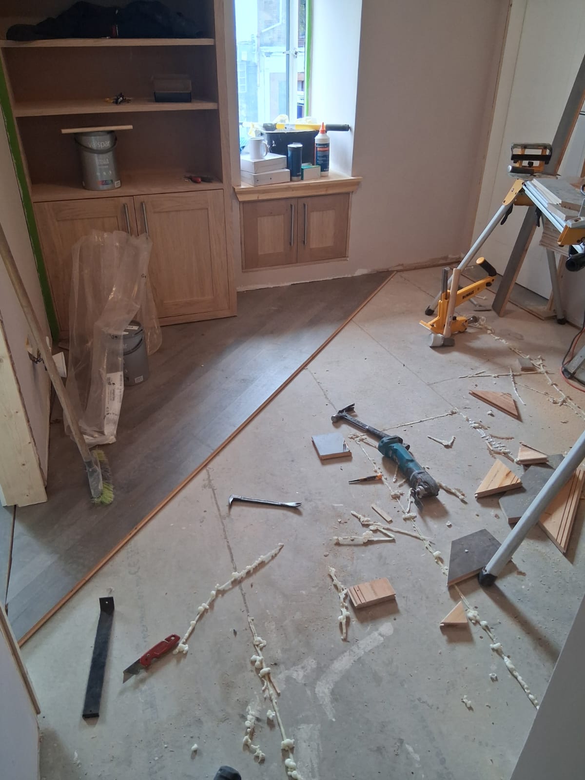 First rows of hardwood flooring laid diagonally from the corner of a room with fitted oak cabinets, with lines of adhesive on the subfloor