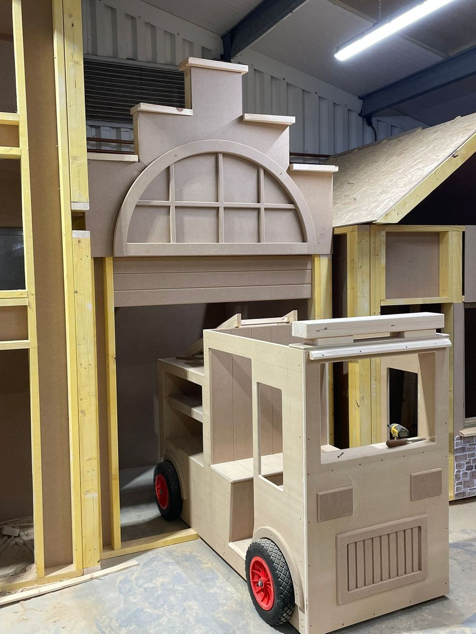 Fire station front with an arched window head being built in the workshop, next to the part-built fire engine unit