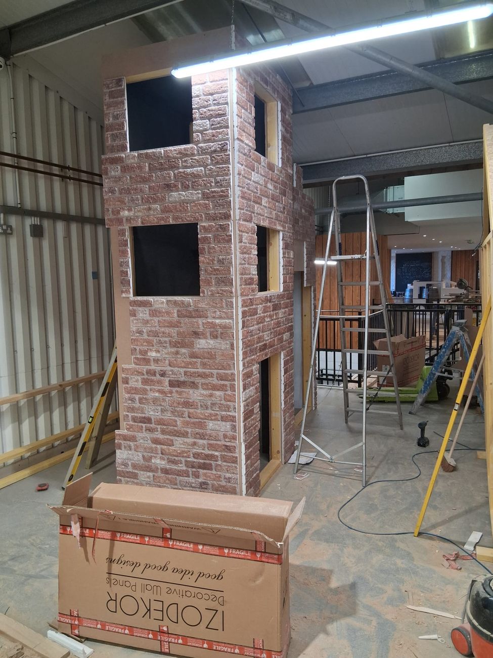 Brick-effect cladding going on to a play building tower with window openings cut out
